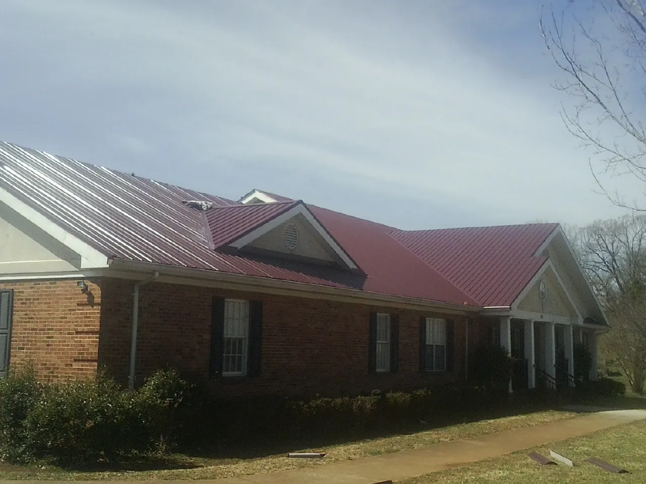 Red metal roof with gabled entries on a long brick building, from a Hail Damage Roof Repair job in Elmwood Park